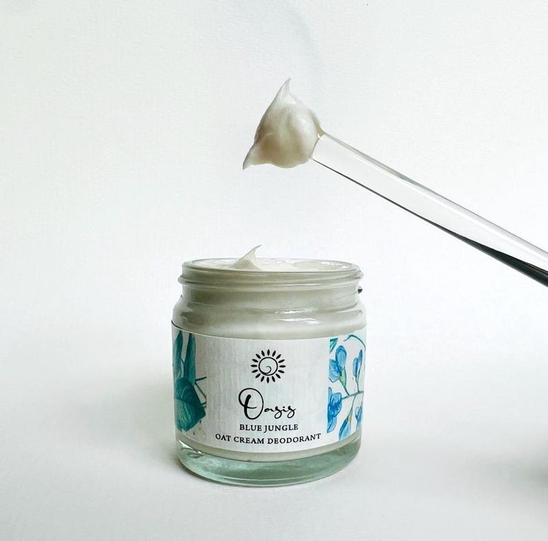 May include: A white jar of Oasis Blue Jungle Oat Cream Deodorant with a blue and green floral design on the label. A small amount of cream is on a clear plastic spatula.