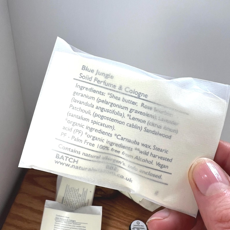 Pu&ograve; includere: Un sacchetto di carta bianco con un'etichetta gialla che recita "Blue Jungle Solid Perfume & Cologne". L'etichetta elenca gli ingredienti, tra cui burro di karit&egrave;, rosa, geranio, lavanda, limone, patchouli, sandalo e cera di carnauba. L'etichetta indica anche che il prodotto &egrave; privo di olio di palma, vegano e contiene allergeni naturali. L'indirizzo del sito web "www.naturalhorizons.co.uk" &egrave; stampato nella parte inferiore dell'etichetta.