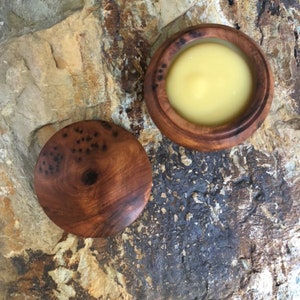 May include: A wooden container with a lid, filled with a pale yellow substance. The container is made of dark wood with a natural grain pattern.