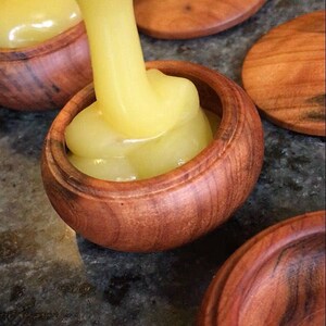 May include: A close-up of a wooden container being filled with a thick, yellow liquid. The container is made of dark wood with a smooth, polished finish. The liquid is pouring from a container off-screen.
