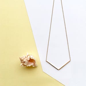 Peut inclure: Un collier en chaîne dorée avec un pendentif en forme de V simple. Le collier est sur un fond blanc et jaune.