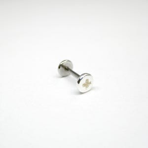 Op de afbeelding: Zilveren schroefvormige oorbel. De oorbel is een kleine, ronde schroef met een platte kop. De schroef is gemaakt van zilver en heeft een glanzende afwerking.