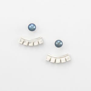 May include: A pair of silver earrings with a curved, geometric design. Each earring features a row of small, square-shaped elements. The earrings are paired with two dark blue pearls.