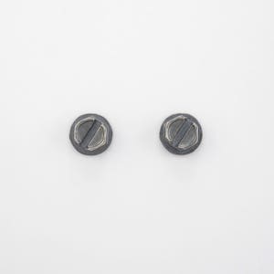 May include: Two small, round, black metal screw heads with a silver slot in the centre.