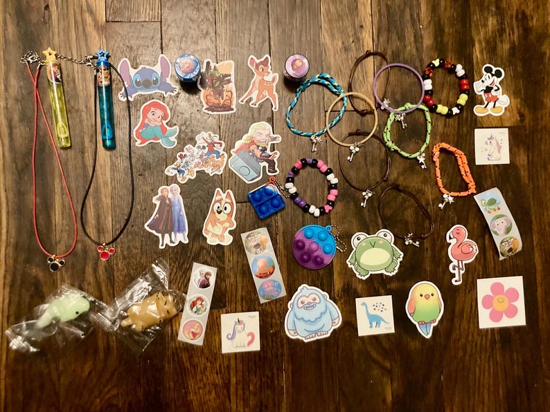 May include: A collection of colorful bracelets, necklaces, and stickers featuring Disney characters like Stitch, Mickey Mouse, and a unicorn. There are also a few small toys, including a frog, a flamingo, and a unicorn.