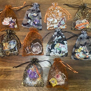 May include: A collection of Halloween-themed gift bags. The bags are made of sheer fabric in various colors, including orange, black, and gray. Each bag features a different Halloween design, such as bats, spiders, and pumpkins. The bags are tied with drawstrings.