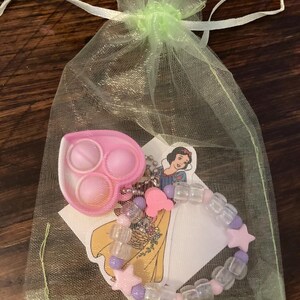 May include: A green mesh bag with a pink heart-shaped pop-it toy, a pink and purple beaded bracelet with star charms, and a sticker featuring Snow White from Disney.
