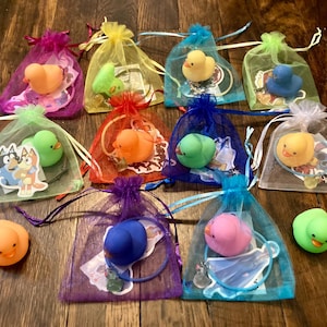 May include: Twelve small, colorful, mesh bags filled with rubber duckies. Each bag has a different color and a different rubber ducky inside. The duckies are yellow, green, blue, pink, and orange.