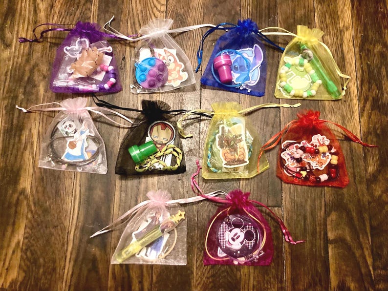 May include: Twelve small organza bags filled with various small toys and trinkets. The bags are tied with ribbons and are arranged in a row on a wooden surface.