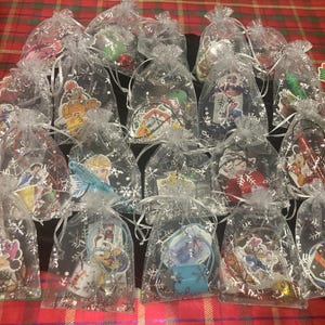 May include: A collection of clear cellophane bags, each tied with a white ribbon and containing a small ornament. The ornaments feature various cartoon characters and holiday-themed designs, perfect for Christmas.