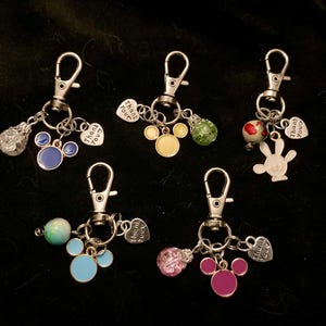 May include: Six silver keychains with different charms. Each keychain has a silver heart charm with the text "Thank You" on it. The charms include a blue Mickey Mouse head, a yellow Mickey Mouse head, a white Mickey Mouse hand, a blue Mickey Mouse head with a light blue bead, a yellow Mickey Mouse head with a pink bead, and a purple Mickey Mouse head with a green bead.