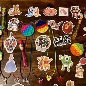 May include: A collection of colorful pop it fidget toys, character stickers, and charm necklaces. The stickers feature characters from popular movies and cartoons, including Star Wars, Mickey Mouse, and Guardians of the Galaxy. The necklaces have charms in the shape of Mickey Mouse ears, a heart, and a star.