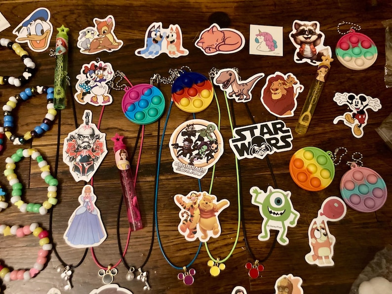 May include: A collection of colorful pop it fidget toys, character stickers, and charm necklaces. The stickers feature characters from popular movies and cartoons, including Star Wars, Mickey Mouse, and Guardians of the Galaxy. The necklaces have charms in the shape of Mickey Mouse ears, a heart, and a star.
