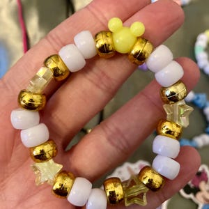 May include: A white and gold beaded bracelet with yellow star and Mickey Mouse charms.