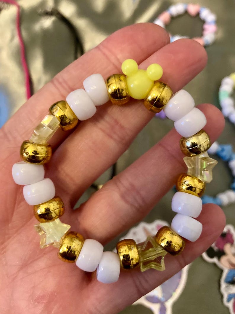 May include: A white and gold beaded bracelet with yellow star and Mickey Mouse charms.