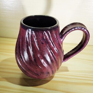 Könnte beinhalten: Eine tiefviolette Keramiktasse mit einem strukturierten, spiralförmigen Design und einem abgerundeten Griff.