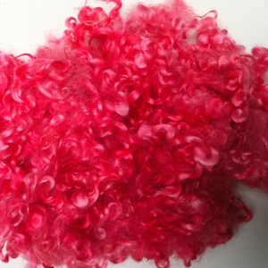 Puede incluir: Fibra de lana rizada de color rosa brillante. La lana tiene una textura suave y esponjosa con rizos apretados e irregulares. El color es un rosa vibrante y saturado, con reflejos rosas más claros. Adecuada para diversos proyectos de manualidades.