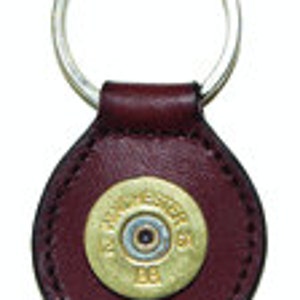 May include: A brown leather keychain with a gold-colored shotgun shell in the center. The shell has the text "12 GA" printed on it.