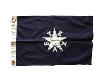 May include: A navy blue flag with a white five-pointed star and the word "TEXAS" spelled out around the star.