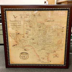 May include: A framed map of Texas with a vintage aesthetic. The map is printed on a cream-colored background with brown lines and text. The map is surrounded by a brown frame with a gold-colored trim.