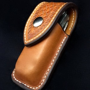 May include: A brown leather pocket knife sheath with a white stitching detail and a decorative embossed pattern. The sheath has a snap closure.