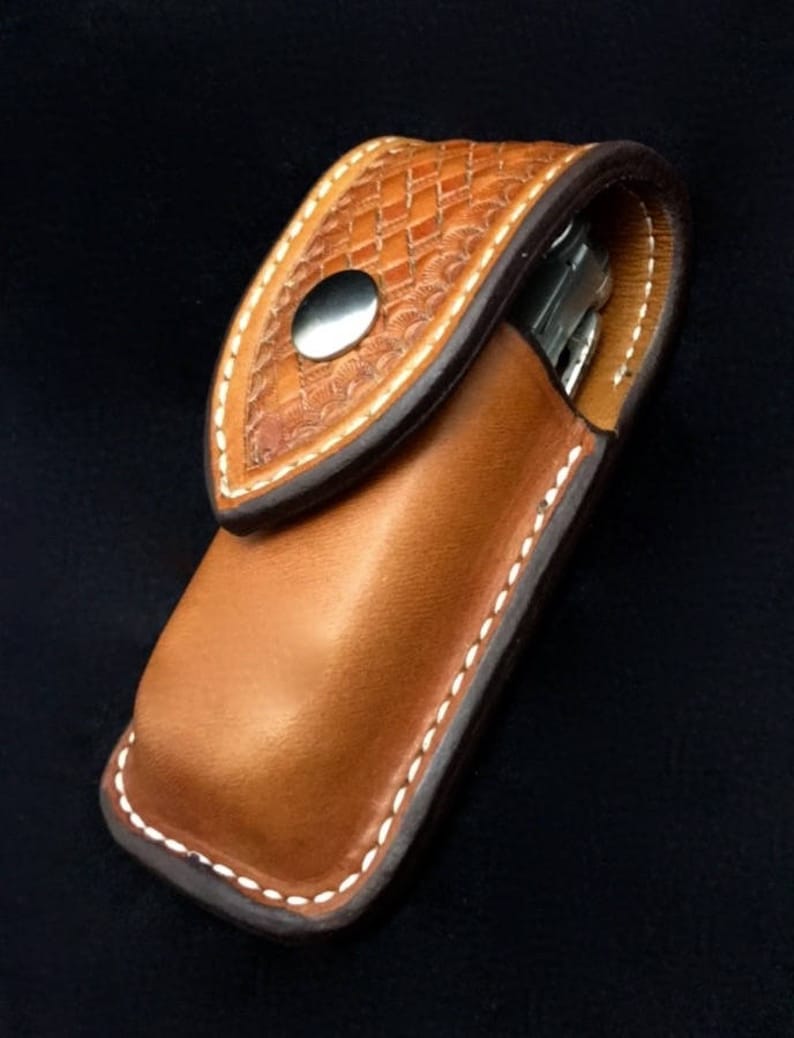 May include: A brown leather pocket knife sheath with a white stitching detail and a decorative embossed pattern. The sheath has a snap closure.