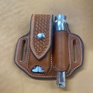 Könnte beinhalten: Eine braune Lederscheide mit einem gestickten Design hält ein silbernes Multitool und eine silberne Taschenlampe.