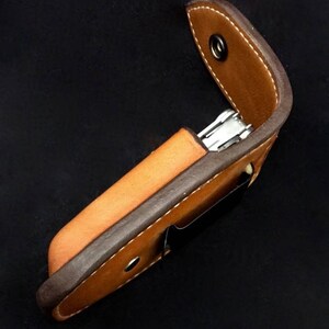 May include: A brown leather case with a snap closure for a multi-tool. The case is made of two pieces of leather, one brown and one dark brown, stitched together.