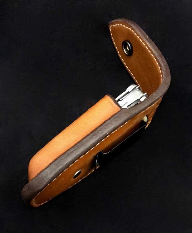 May include: A brown leather case with a snap closure for a multi-tool. The case is made of two pieces of leather, one brown and one dark brown, stitched together.