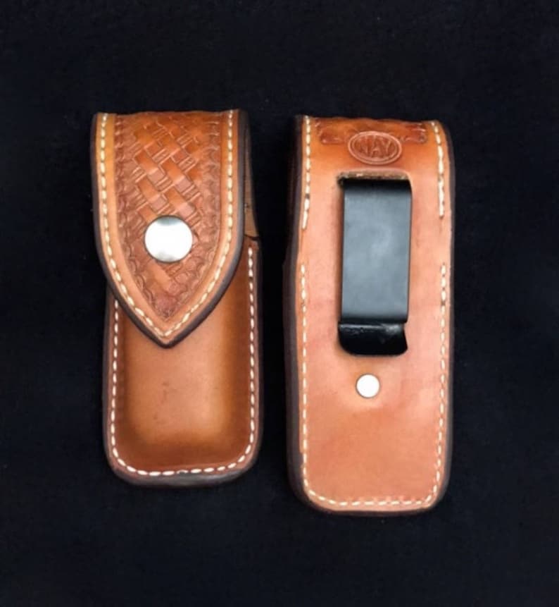 May include: Two brown leather knife sheaths with white stitching. One sheath has a woven pattern and a silver button. The other sheath has a black clip and the word "WAY" embossed on the front.