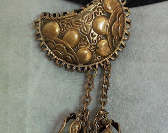 May include: A gold-toned metal pendant with a decorative, ornate design and a chain with multiple dangling bells.