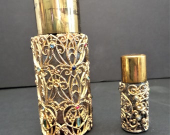 May include: Two gold-toned perfume bottles with intricate filigree designs and colorful gemstones. The larger bottle is taller and has a gold cap. The smaller bottle is shorter and has a gold cap.