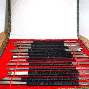 May include: A set of 10 metal carving tools with black handles and red string ties, arranged in a green and red velvet lined box.