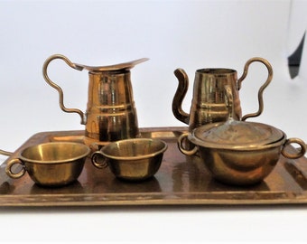 May include: A miniature brass tea set on a brass tray. The set includes a teapot, creamer, sugar bowl, and two cups.