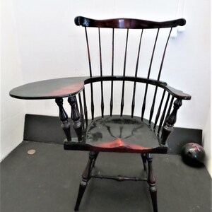 May include: A black and red wooden chair with a small side table attached to the left armrest. The chair has a high back with vertical spindles and a curved seat.