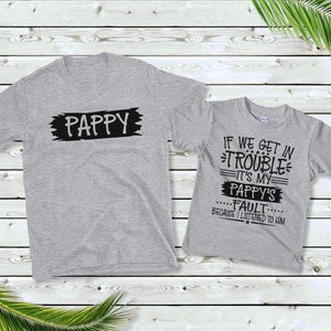 May include: Two gray t-shirts with black text. The larger shirt says "Pappy" in a black rectangle. The smaller shirt says "If we get in trouble it's my Pappy's fault because I listened to him".