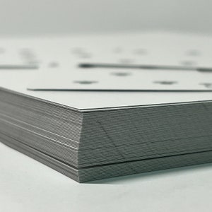 May include: A stack of white cards with black edges. The cards are neatly aligned and the edges are visible.