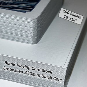 May include: A stack of 100 blank playing card stock sheets, measuring 12" x 18". The sheets are embossed and have a black core. The text "Blank Playing Card Stock Embossed 330gsm Black Core" is printed on the bottom of the stack.