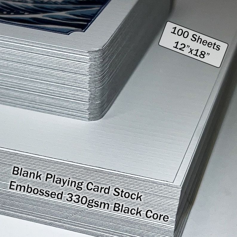 May include: A stack of 100 blank playing card stock sheets, measuring 12" x 18". The sheets are embossed and have a black core. The text "Blank Playing Card Stock Embossed 330gsm Black Core" is printed on the bottom of the stack.