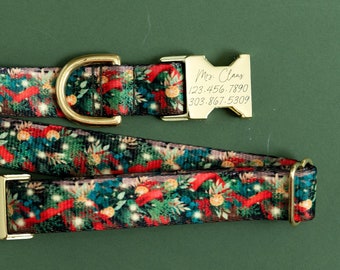 Puede incluir: Un collar de perro dorado con un patrón navideño que presenta ramas de pino, cintas rojas y luces. El collar tiene una hebilla dorada con una etiqueta personalizada que dice "Mr. Claus 123-456-7890 303-867-5309".