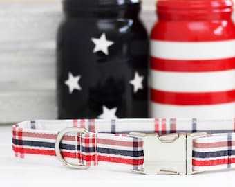 Puede incluir: Collar de perro de cuadros rojo, blanco y azul con una hebilla plateada. El collar está sobre una superficie blanca delante de tres tarros decorados con rayas rojas, blancas y azules.