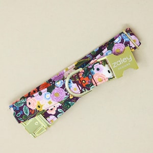 以下が含まれることがあります： 紫、ピンク、青の花柄の犬用首輪。 金色の金具と、金色のタグに「zaley designs」の文字が入っています。 ペット用のアクセサリーです。