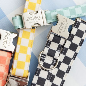 May include: Four dog collars with different checkered patterns. The collars are all made of fabric and have silver buckles with the text "Zaley Designs" engraved on them.