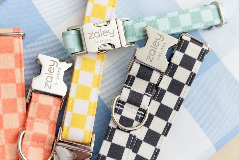 May include: Four dog collars with different checkered patterns. The collars are all made of fabric and have silver buckles with the text "Zaley Designs" engraved on them.