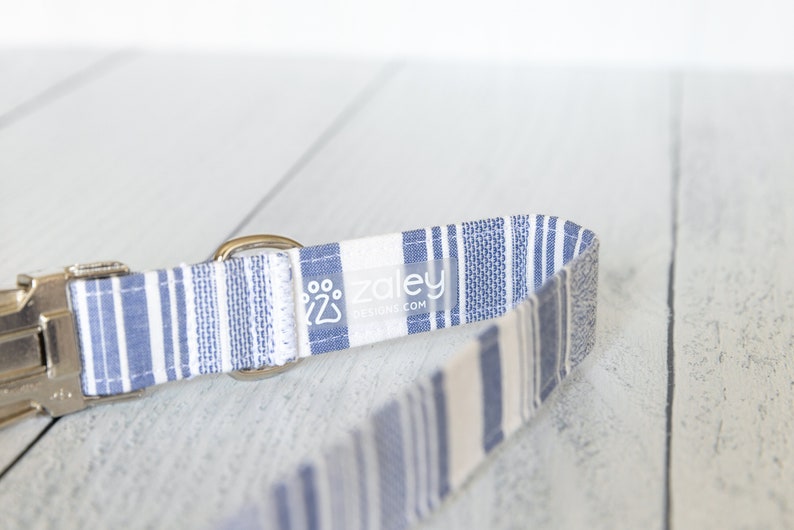 May include: A blue and white striped dog collar with a silver buckle and a white label that says "zaley designs.com".