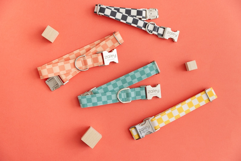 May include: Four dog collars with a checkered pattern in different colors: black and white, peach, teal, and yellow. The collars have silver buckles with the word "Zaley" printed on them.