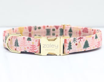 Puede incluir: Un collar para perro rosa con una hebilla dorada con el texto "zaley designs" y un patrón festivo de árboles de Navidad.