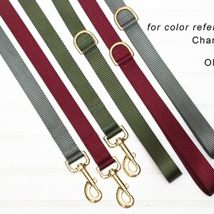 May include: Five dog leads in different colours: charcoal grey, burgundy, olive green, grey, and burgundy. The leads are made of a woven nylon material and have gold-coloured metal clasps.  "for colour reference only" is written in black text at the top of the image.  "Charcoal Grey", "Burgundy", and "Olive Green" are written in black text below the leads.