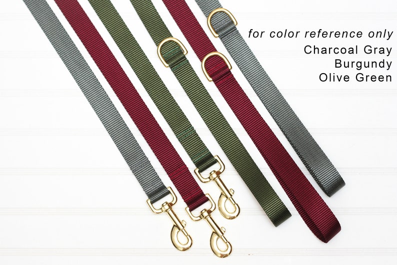 May include: Five dog leads in different colours: charcoal grey, burgundy, olive green, grey, and burgundy. The leads are made of a woven nylon material and have gold-coloured metal clasps.  "for colour reference only" is written in black text at the top of the image.  "Charcoal Grey", "Burgundy", and "Olive Green" are written in black text below the leads.