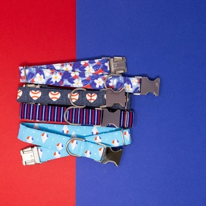 Puede incluir: Una pila de cinco collares de perro coloridos con diferentes patrones, que incluyen flores, b&eacute;isbol, rayas y conos de helado. Los collares son todos azules y blancos con hebillas plateadas.
